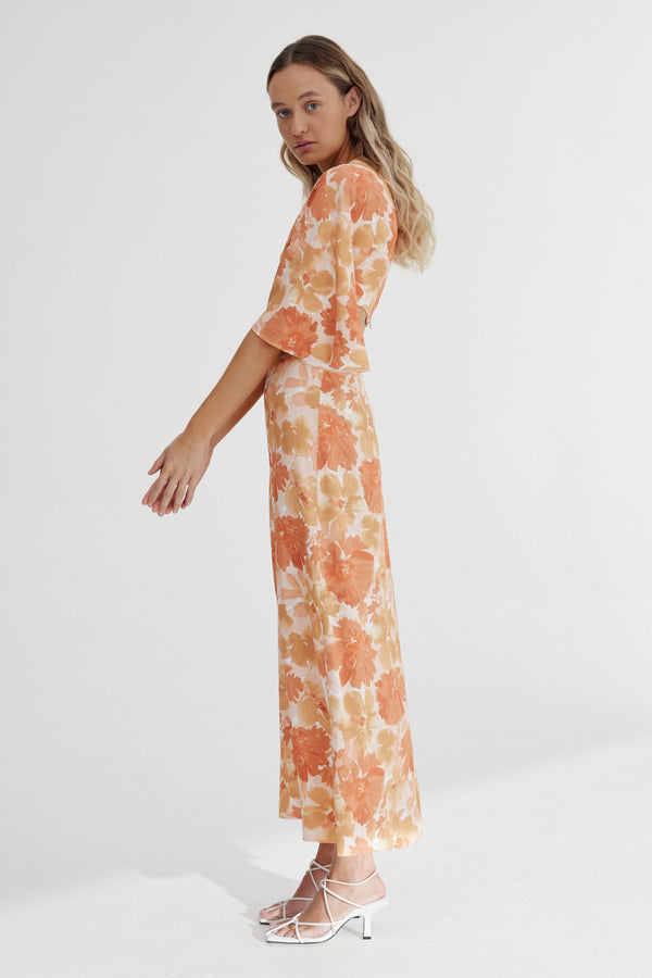 A side view of a model standing against a white background wearing Significant Other's Maeve Midi Dress in Scarlet Poppy Floral.