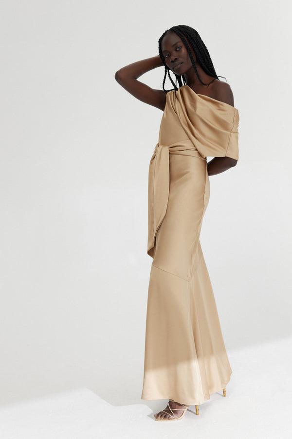 A side view of a model with one hand behind their head and back standing against a white background wearing Significant Other's Erika dress in Tan.